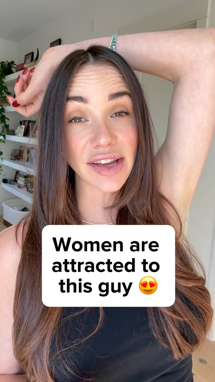 A woman with long brown hair is centered in the frame, smiling and looking directly at the camera. She is wearing a black top. Overlayed on her image is a white rectangle containing the text 'Women are attracted to this guy' above a heart-eyes emoji.