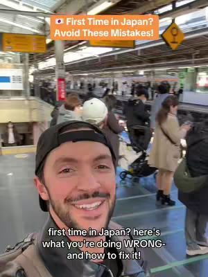 A man is smiling at the camera in a busy train station setting. Behind him are blurred figures and signs. The overlaid text indicates the video is about avoiding mistakes on a first trip to Japan.