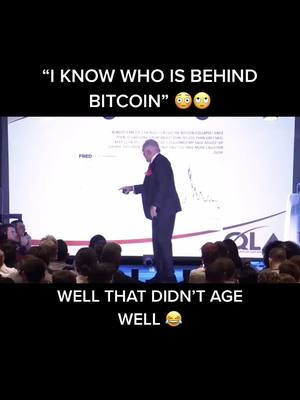 The cover image shows a man in a suit pointing to a screen from a stage. Above him, text says, “I KNOW WHO IS BEHIND BITCOIN,” and below, other text states, “WELL THAT DIDN’T AGE WELL.” The image depicts a lecture hall setting with an audience. The composition is a medium shot, and the lighting is neutral.