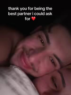 A close-up shot of a couple in bed, with one person's face prominently in focus against a dark background. The other person is partially visible, resting on the first person's shoulder. Overlayed text is visible above the faces.