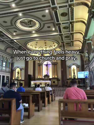 An interior shot of a church, with a high ceiling and rows of wooden pews. Sunlight streams in from the windows, and several people can be seen sitting in the pews. The focus of the image is on the church's architecture and the presence of people.