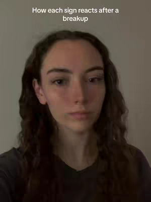 A close-up shot featuring a young woman with long, wavy dark hair, positioned centrally. The background is a softly lit, gradient gray. The woman has a neutral expression.