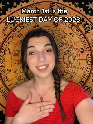 A woman with a braid in her brown hair is centered in front of a circular background featuring astrological symbols. The woman is smiling, wearing red clothing, and has a necklace and ring on. Text at the top reads 'March 1st is the Luckiest Day of 2023!'