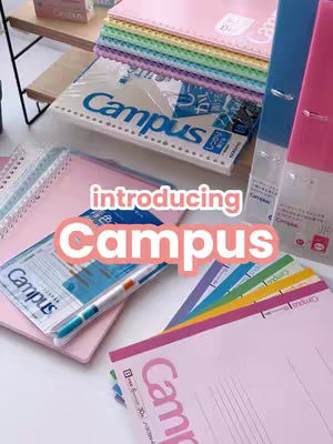 The image showcases various stationery and office supplies. The composition includes notebooks, binders, and pens arranged on a surface, likely a desk. The color palette is bright and appealing, with soft pinks, blues, and a rainbow of colors.
