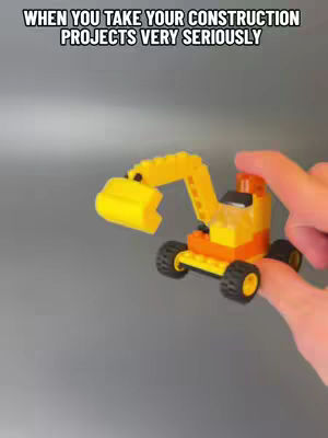 The image shows a LEGO model excavator held by a pair of hands against a grey background. The excavator is predominantly yellow and orange with black wheels. Text overlays the image.