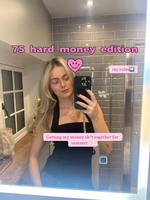 A woman taking a selfie in a bathroom mirror. The background includes light gray tiles and a window. The woman is blonde and wearing a black top. Text overlays include "75 hard money edition", "my rules ->", and "Getting my money sh*t together for summer".