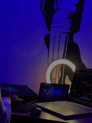 The image captures a dimly lit space where a person appears to be trading stocks on multiple laptops. Three laptops are open on a dark surface, displaying stock charts and graphs, lit by a ring light. Behind the laptops, there is a large wall graphic. The silhouette of a person's arm and hand is visible on the left, interacting with one of the laptops. The color palette is dominated by blues and greens. The lighting is suggestive of a studio setting aimed at recording a tutorial.