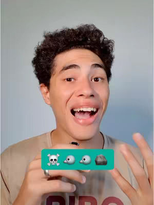 A young man with dark, curly hair and a tan shirt is smiling widely, showing his teeth. He has a background of a solid light gray-blue color. In front of him, he's holding a teal rectangle featuring a skull emoji, two bird emojis and a rock emoji.