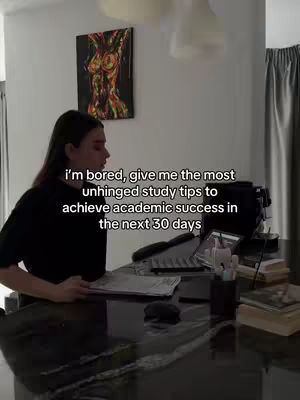 A woman is sitting at a desk with a laptop, papers, and pens. Text overlayed on the image reads: 'I'm bored, give me the most unhinged study tips to achieve academic success in the next 30 days'. A painting hangs on the wall in the background.