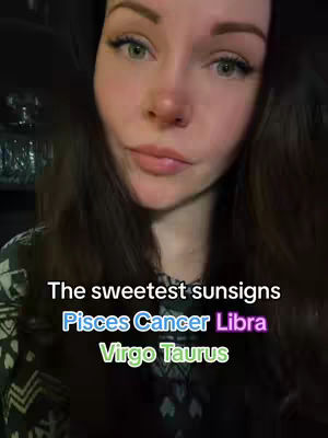 A woman with long brown hair, light skin, and green eyes is centered in the frame, looking towards the camera with a slight, almost knowing smile. The background is dark, possibly an interior space. Text overlays appear with colorful fonts. The woman is wearing a dark patterned top.