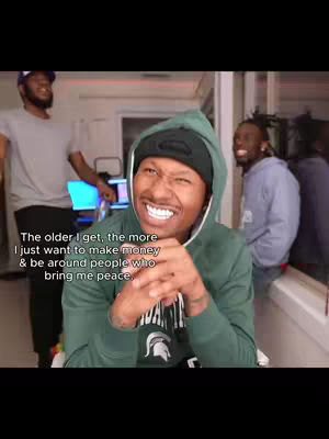 A man wearing a green hoodie and a black beanie smiles at the camera. Text is overlaid on the image. Two other men are partially visible in the background.