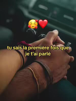 Close-up shot of two pairs of hands holding each other. The background is blurred, suggesting an intimate setting, possibly inside a car, with the dashboard visible. Text in light yellow overlay reads 'tu sais la première fois que je t'ai parlé'. Emojis of a smiling face with hearts and a red heart are laid on the background.