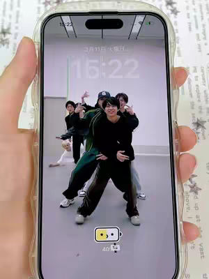 The cover image shows a person holding a smartphone displaying a lock screen and background image. The background image is a group of six men in what appears to be a dance studio. They are in various dance poses. The phone is in a clear case, and the person holding the phone is partially visible. The time and date are shown on the phone's screen. The phone's battery icon is also visible, indicating it is at 46%.