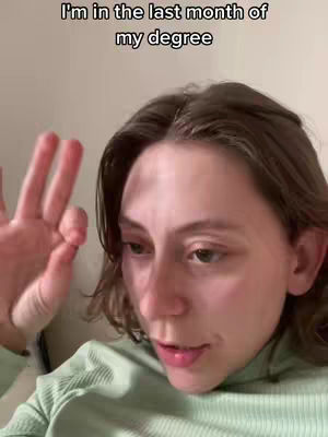 A close-up shot of a woman, likely indoors. She has light skin, brown hair, and is wearing a light green, ribbed, long-sleeved top. The text overlay, prominently displayed, reads, 'I'm in the last month of my degree.' The woman's expression suggests a mix of contemplation and perhaps a touch of weariness. There is an okay hand gesture made by the woman.