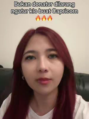 The cover image features a woman with long, maroon hair looking directly at the camera. She is wearing a white shirt and is positioned against a plain background, possibly a wall or a simplistic indoor setting. Above her, overlaid text is displayed with three flame emojis. Her expression is neutral, and the composition is a medium shot, focusing on her face and upper body.