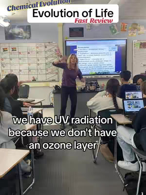 A classroom scene with a female teacher lecturing in front of a large screen displaying educational content. Students are seated at desks, and overlaid text is displayed at the bottom of the image.