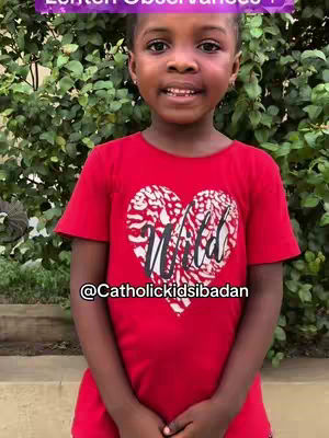 A young girl in a red t-shirt with a white heart design stands in front of a green leafy background. She smiles at the camera, and text overlays are present on the image.