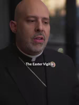 The image shows a close-up of a man wearing a clerical collar, looking slightly to the side. The overlaying text says "The Easter Vigil is". He appears to be indoors, with blurred background elements suggesting a professional setting.