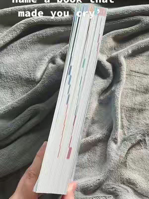 A hand holds a stack of book pages, fanned out to display the colorful edges of the pages. The hand is on a grey, heavily textured surface.