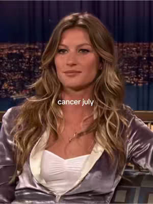 A portrait of a woman with long wavy blonde hair and fair skin. She is wearing a purple jacket over a white top. The background is blurred, but appears to be a nighttime cityscape. The text overlay reads 'cancer july'.