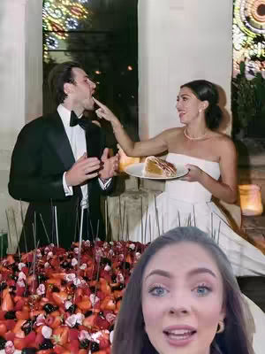 The image is composed of multiple layers. In the background, a well-lit space with architectural features. Centered is a wedding scene: a couple, the woman in a strapless white dress, placing a finger with cake on the man's mouth. Foreground layer includes a large cake covered in different fruits. In the bottom right corner, a woman faces the camera, with a surprised expression.