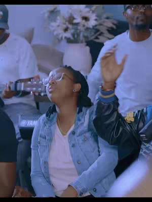 A medium shot shows a group of people in what appears to be a worship setting. A woman with glasses is in the foreground, her face tilted upward, and her hands raised in worship. Others are visible in the background, some holding instruments.