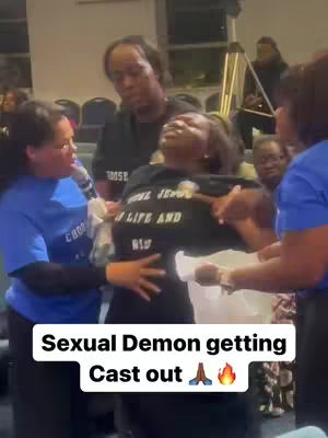A group of people gathered indoors with an image overlay. A person is being held by others. The person in the center has their head tilted back, with a look of expression. Others around them are supporting and holding them. The overlayed text is white and includes the word 'Sexual Demon'.