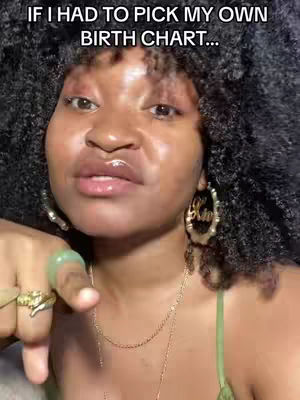 A close-up shot of a woman with dark, curly hair, looking at the camera. The image is well-lit, with a focus on her face, and the background is blurred. She is wearing gold hoop earrings with text inscribed on them, a green ring, and multiple gold rings. She's also wearing a gold necklace and a green top.