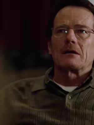 A close-up shot of a man wearing glasses and a collared shirt. He appears to be looking off to the side with a somewhat concerned expression.
