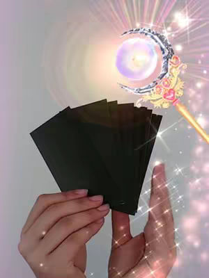 A person's hands are holding a stack of black cards, with hands to the right holding a magical wand, with a moon design, a glowing orb, surrounded by radiating lines and sparkles.