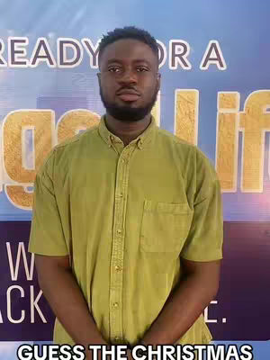 A medium shot of a Black man in an olive green button-down shirt. The background is a light blue with the words 'READY OR A BIG LIFE' in white and the word 'G' in yellow. At the bottom of the image is the text 'GUESS THE CHRISTMAS'.