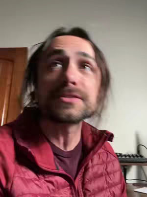 A man looking up at the camera with a concerned expression. He is wearing a red jacket.