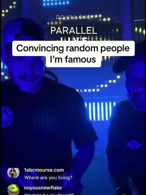 The image features two men, one in a dark hoodie and the other one in a black t-shirt. They are in a dimly lit room with blue and yellow lights. Text overlays state 'DOWNLOAD' and 'PARALLEL LIVE'. A white rectangular box contains the text 'Convincing random people I'm famous.' The background is dark, with visible lines of light above the subjects.