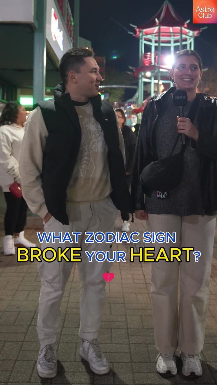 Two people are standing outside at night. A man on the left is smiling and talking. A woman on the right is holding a microphone and smiling. Text on the image asks, 'What zodiac sign broke your heart?'
