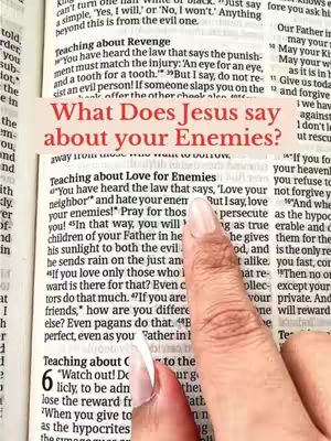 An open Bible is shown with a highlighted passage featuring the question "What Does Jesus Say about your Enemies?" A hand with polished nails is pointing at the text. The background shows more text from the Bible.