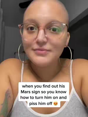 A close-up shot of a bald woman with glasses and hoop earrings. She's centered in the frame, looking towards the camera. A text overlay appears at the bottom, written in a white font against a white rectangle.