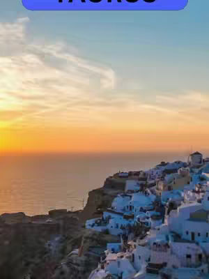 A scenic landscape featuring white buildings on a cliff overlooking the ocean, bathed in the warm light of a sunset. The sky transitions from blue to orange, creating a serene and picturesque setting.