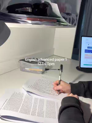 A person writing at a desk with papers and a laptop, the image framed from a top-down perspective. A pencil case and writing tools are placed on the desk, with text overlaid at the bottom.