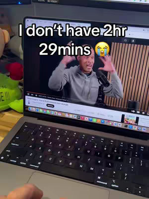A laptop is open on a desk, displaying a video of a man speaking. Above the video, overlaid text reads, "I don't have 2hr 29mins," with a crying emoji. The laptop screen shows a YouTube video, and the keyboard and a hand are visible.