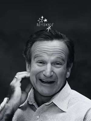 A grayscale photo featuring Robin Williams, the actor, looking at the camera with a smile. He is wearing a collared shirt, has a ring on his finger, and is touching his neck. Above his head is a small illustration of stars with the word "BETTERSELF" written near them.