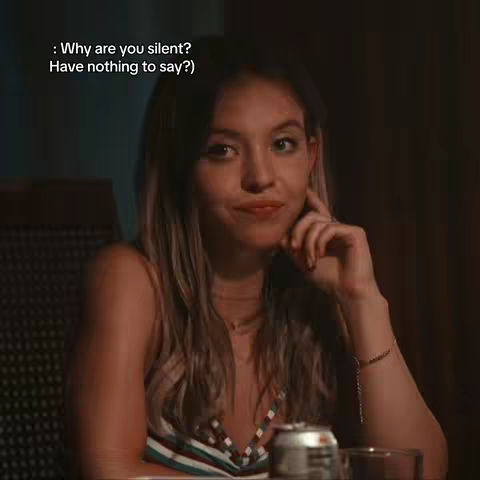 The cover image features a young woman with long, wavy hair, seated and gazing at the viewer with a subtle, questioning expression. She is lightly smiling with a playful expression. The lighting suggests a dimly lit indoor setting, with a can and a drinking glass are partially visible on the table in front of her.