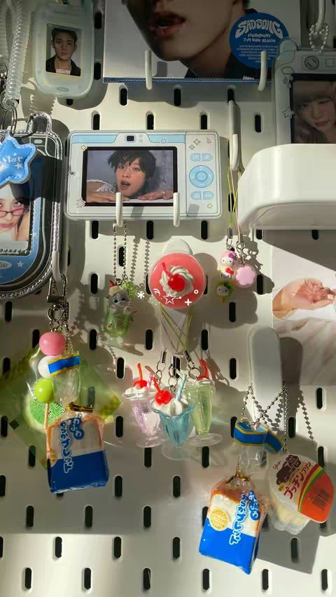 The image is a close-up view of a white pegboard. Hanging on the pegboard are various decorative items, including keychains, small framed photos of people, and miniature food and drink replicas. The items are arranged in a visually appealing way, with a mix of colors and textures. The composition is detailed and captures the essence of decorative items.