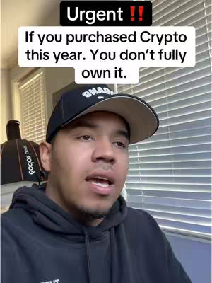 A casual selfie-style shot featuring a man in a black hoodie and a black baseball cap. White text boxes overlay the image, with a message about crypto ownership. The background consists of a window with blinds and some visible office equipment. The composition is straightforward, giving the viewer a direct and informational feel.