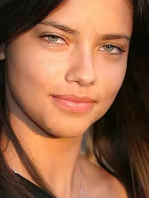 A close-up shot of a woman's face. She has dark hair, fair skin, and light eyes. She is looking slightly to the side with a subtle smile.
