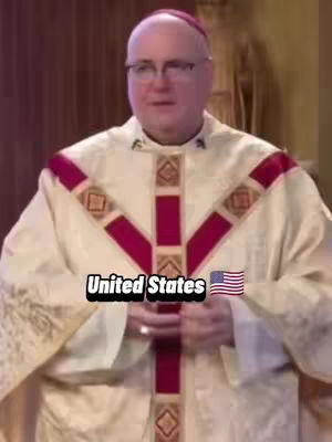 An older man wearing a robe with a burgundy cross-shaped design holds his hands in front of him. A text overlay at the bottom center of the image reads "United States" with an American flag graphic next to it. The background is slightly blurred but seems to be indoors.