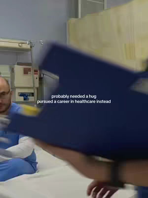 The cover image is a vertical shot, likely taken in a hospital or medical setting, judging by the background. Two people are visible. One, a person wearing glasses and medical scrubs, is partially visible on the left, looking toward the frame. The other person’s arms are partially visible holding a blue device, partially obscuring the view. Behind them is a hospital bed and medical equipment, with the text overlay giving context.
