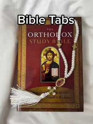 The cover image displays an open book with a religious theme. The central focus is on a book labeled 'The Orthodox Study Bible,' with an illustration of a religious figure. Overlaid on the book is a white beaded rosary. Above the book, the words 'Bible Tabs' are clearly visible. The background is a soft off-white, providing a subtle contrast to highlight the book and rosary. The overall composition suggests spiritual study.