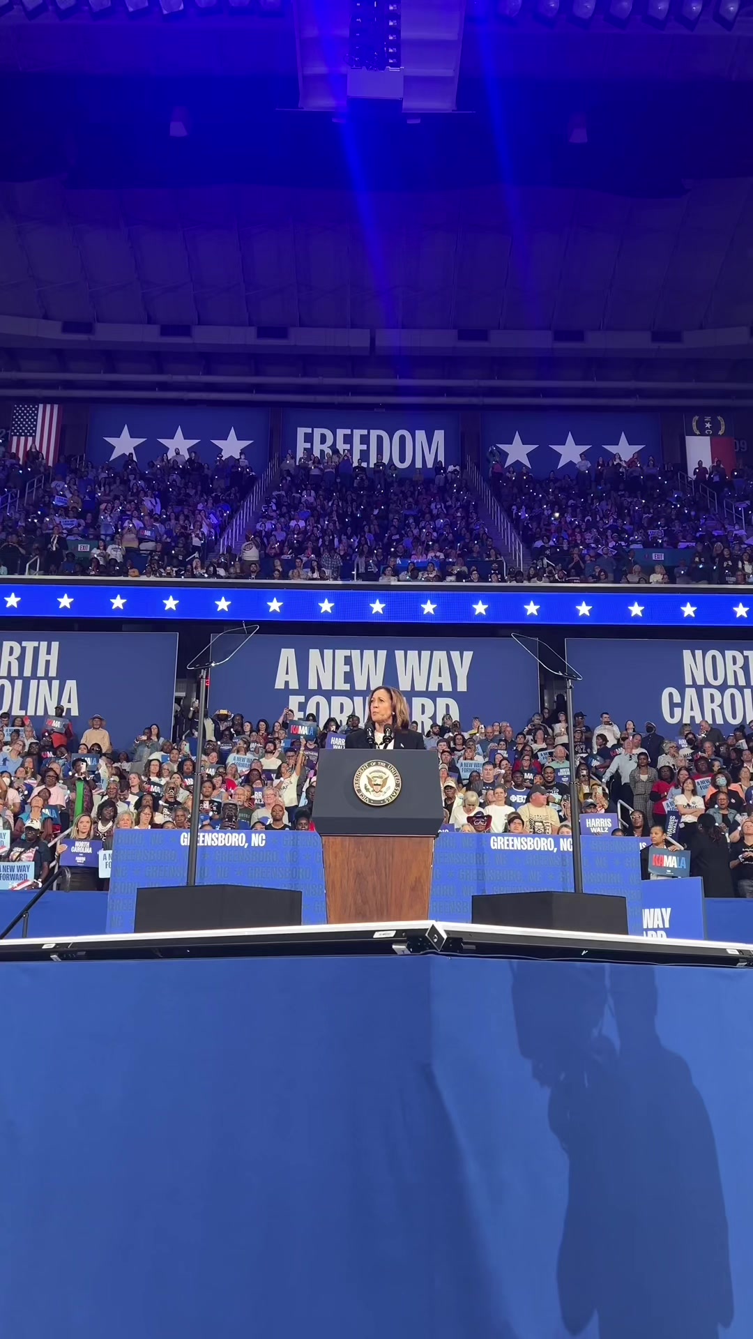 The cover image shows a view of a large indoor event, presumably a political rally, with a woman, clearly the main subject, speaking at a podium. The background is filled with a crowd of people, and the stage has supportive signage. The color scheme is dominated by shades of blue with accents of white and red, and the layout is symmetrical, with a central focus on the speaker and the audience in the back.