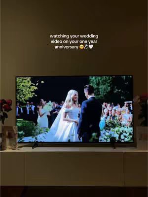 The image features a television screen displaying a wedding scene. In front of the screen is a low, white cabinet. The hook text is at the top of the image. The TV screen shows a couple at their wedding, illuminated by natural light or soft lighting. The composition is simple, focusing on the TV screen and the hook text providing context and sentiment.