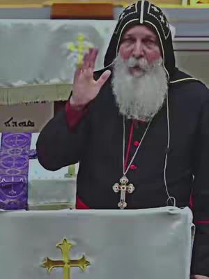 The cover image features a man with a white beard wearing a black hooded robe and a cross necklace, gesturing with his right hand in a church setting. A golden cross is visible on the table.